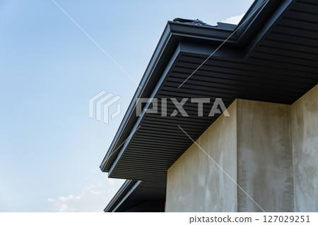 A close view of a metallic tile roofing installation on a modern building, showcasing craftsmanship and design under a bright sky 127029251