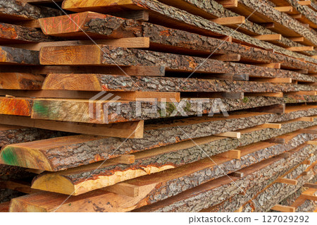 A collection of neatly stacked wooden planks reveals rich textures and colors, illustrating woodworking materials at a lumber yard 127029292