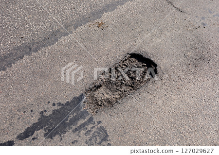 A large pothole is present on an asphalt road, creating obstacles for vehicles in a residential neighborhood during the daytime A large pothole is present on an asphalt road, creating obstacles for vehicles in a residential neighborhood during the daytime 127029627