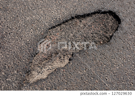 A large pothole is visible in an asphalt street, posing risks for vehicles and pedestrians navigating the area 127029630