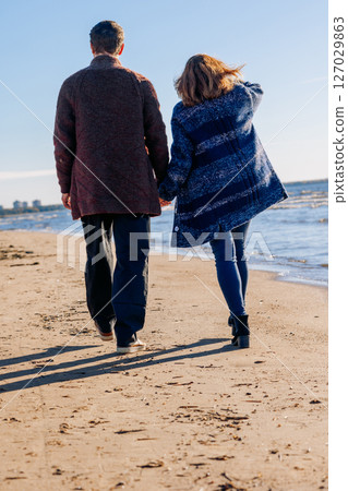 Loving couple walks on beach along sea on sunny autumn day. Weekend and lifestyle concept. Vertical photo. Back view. High quality photo 127029863
