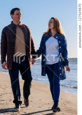 Loving couple walks on beach along sea on sunny autumn day. Weekend and lifestyle concept. Vertical photo. High quality photo 127029870