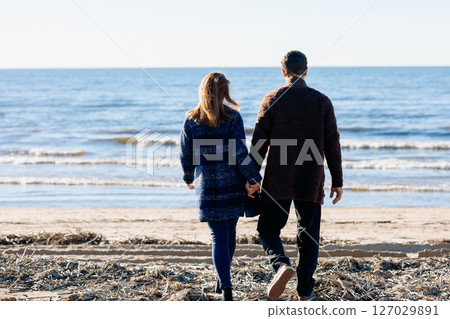 Loving couple walks on beach along sea on sunny autumn day. Weekend and lifestyle concept. Back view. High quality photo 127029891
