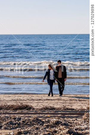 Loving couple walks on beach along sea on sunny autumn day. Weekend and lifestyle concept. Vertical photo. High quality photo Loving couple walks on beach along sea on sunny autumn day. Weekend and lifestyle concept. Vertical photo. High quality photo 127029898