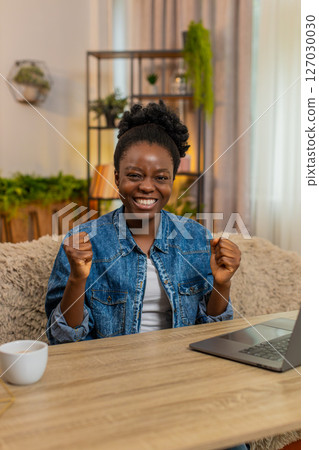 African American woman celebrates success after finishing laptop work, happy victory gesture at home 127030030