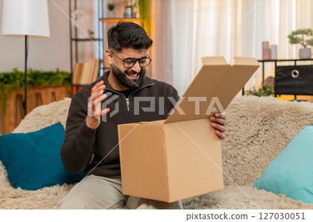 Indian man on sofa opens box and shakes head after discovering wrong item in online delivery order 127030051