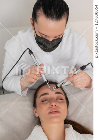 Beautician doctor makes woman micro currents face therapy using electrical impulses in spa salon 127030054