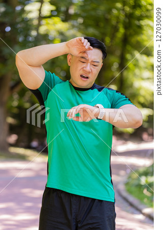 Tired Japanese runner fitness man using smartwatch bracelet watch checking result heartbeat in park Tired Japanese runner fitness man using smartwatch bracelet watch checking result heartbeat in park 127030099