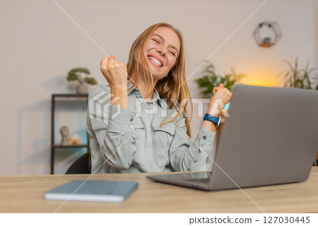 Excited Caucasian woman working on laptop shocked by sudden victory sitting at home office desk Excited Caucasian woman working on laptop shocked by sudden victory sitting at home office desk 127030445