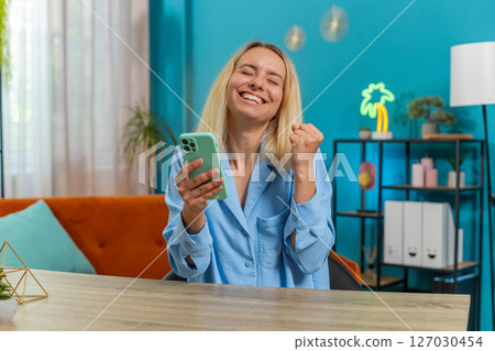 Woman freelancer using mobile smartphone receive good news celebrate victory win at home office Woman freelancer using mobile smartphone receive good news celebrate victory win at home office 127030454