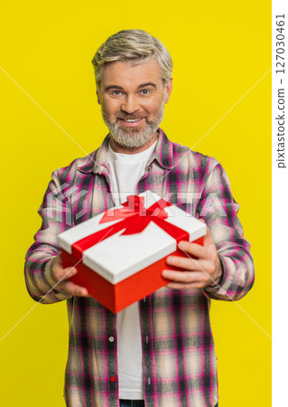 Mature man gifting box with red ribbon, joyful smile gesture, celebration mood birthday surprise 127030461