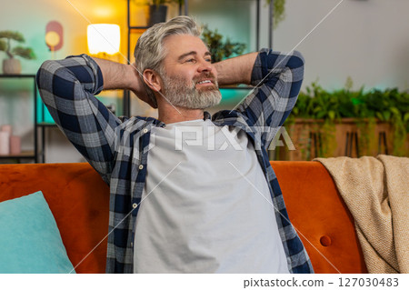Tired senior middle-aged man stretching arms and resting relaxing on sofa in living room at home Tired senior middle-aged man stretching arms and resting relaxing on sofa in living room at home 127030483