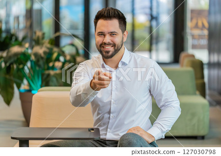 Portrait of Caucasian young businessman pointing to camera choosing hire sitting in office lobby 127030798