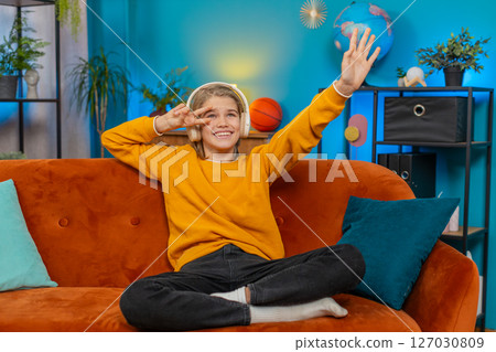 Teenager boy dancing on sofa at home with wireless headphones, enjoying music, moving to rhythm Teenager boy dancing on sofa at home with wireless headphones, enjoying music, moving to rhythm 127030809