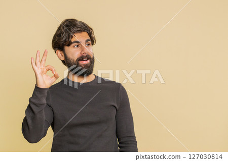Joyful happy Lebanese man in long sleeves looking approvingly at camera against beige background 127030814