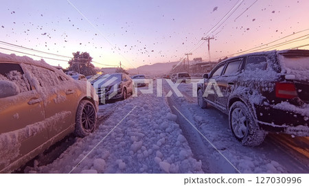 Cars covered in snow are parked on a snow-filled street at sunset. Concept of winter weather and urban life. 127030996