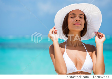 Woman in White Bikini and Hat Enjoys Sunny Beach Day Near Turquoise Ocean Waters 127032344