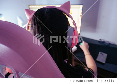 Asian girl with pink headphones playing computer games Asian girl with pink headphones playing computer games 127033115