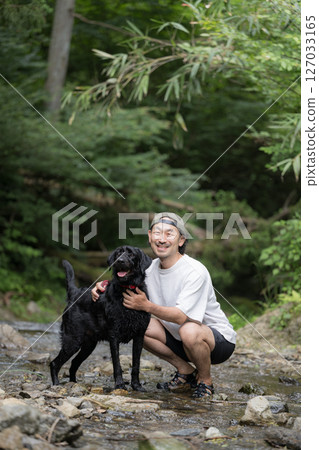 A large dog and its owner playing in the river. A dog that gets hot easily plays in the river in summer. 127033165