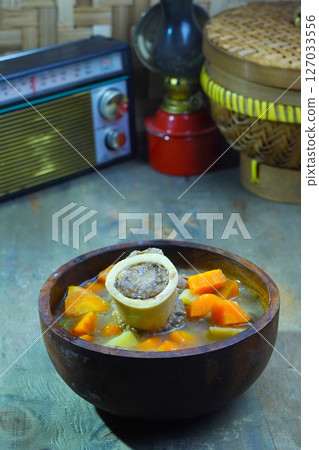 A rich bone marrow soup with chunks of carrots and meat, served in a rustic wooden bowl. A rich bone marrow soup with chunks of carrots and meat, served in a rustic wooden bowl. 127033556