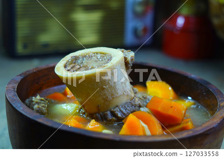 A rich bone marrow soup with chunks of carrots and meat, served in a rustic wooden bowl. A rich bone marrow soup with chunks of carrots and meat, served in a rustic wooden bowl. 127033558