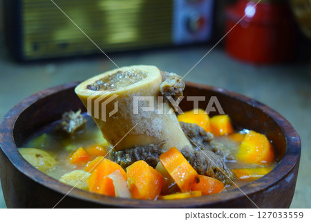 A rich bone marrow soup with chunks of carrots and meat, served in a rustic wooden bowl. A rich bone marrow soup with chunks of carrots and meat, served in a rustic wooden bowl. 127033559