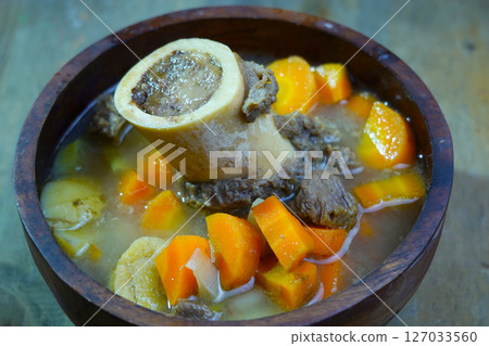 A rich bone marrow soup with chunks of carrots and meat, served in a rustic wooden bowl. A rich bone marrow soup with chunks of carrots and meat, served in a rustic wooden bowl. 127033560