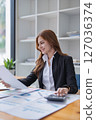 Attractive woman reviews financial documents and calculates figures at desk. 127036374