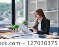 Elegant businesswoman analyzes financial reports at her office desk inside. 127036375