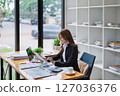 Young businesswoman reviews paperwork while working on laptop in office space 127036376