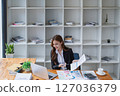 Young businesswoman analyzes financial reports at her office workstation. 127036379