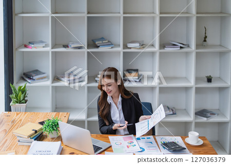 Young businesswoman analyzes financial reports at her office workstation. Young businesswoman analyzes financial reports at her office workstation. 127036379