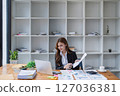 A young businesswoman reviews financial reports while working at her desk office. 127036381