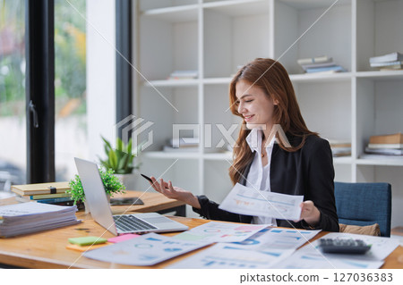 Young business woman analyzes financial reports at her office workplace. Young business woman analyzes financial reports at her office workplace. 127036383