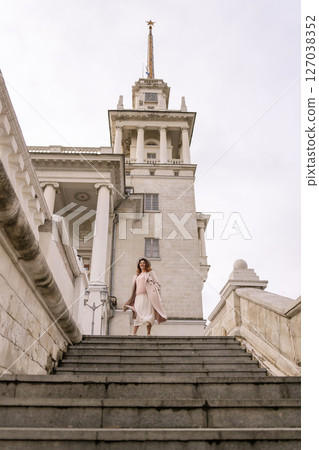 woman in elegant coat and hat against an intricate architectural backdrop, harmoniously blending modern fashion with historical allure. The soft daylight adds to its timeless appeal. 127038352