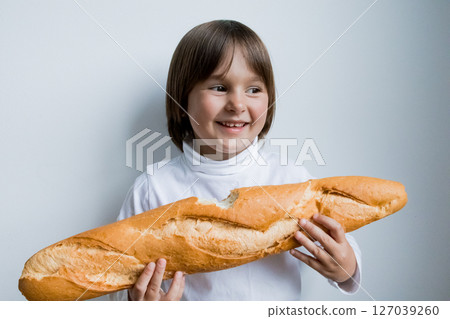 Young caucasian child smiling holding baguette against white background Young caucasian child smiling holding baguette against white background 127039260