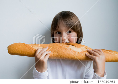 Young caucasian child holding large baguette with curious expression 127039263