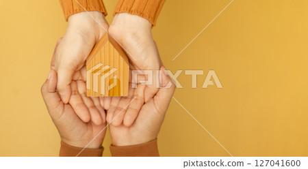 Couple hands holding a yellow wooden house, symbolizing love, home, and starting a family together with warmth and unity Couple hands holding a yellow wooden house, symbolizing love, home, and starting a family together with warmth and unity 127041600