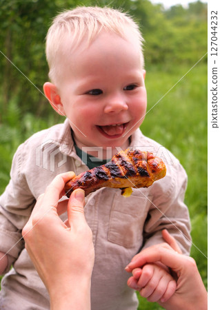 Happy toddler excited about grilled chicken at picnic Happy toddler excited about grilled chicken at picnic 127044232