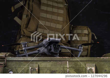 Drone with camera. Drone with three lenses. Quadcopter against the background of a military backpack. 127044296