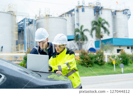 Couple petrochemical workers or technician use laptop on back of car for working in workplace area of factory. Couple petrochemical workers or technician use laptop on back of car for working in workplace area of factory. 127044812