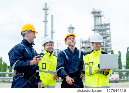 Four petrochemical workers or technicians work together with one hold laptop and they stand in front the factory. 127044816
