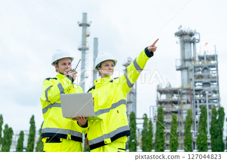 One petrochemical or gas factory worker use walkie talkie to contact other coworker with coworker woman point to their left side in front of factory building. One petrochemical or gas factory worker use walkie talkie to contact other coworker with coworker woman point to their left side in front of factory building. 127044823