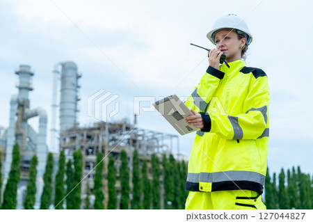 Petrochemical worker or technician woman hold laptop use walkie talkie to contact coworker and stay in front of the factory. 127044827