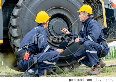Two factory workers sit near wheel of truck and check or maintenance in workplace area. 127044829