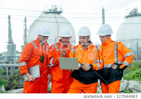 Group of gas factory technicians or  engineers with one hold laptop and discuss together about their work and stay in front of tank with day light. Group of gas factory technicians or  engineers with one hold laptop and discuss together about their work and stay in front of tank with day light. 127044863