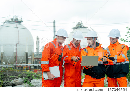 Gas factory workers or  engineers with one hold laptop and discuss together about their work and stay in front of tank with day light. Gas factory workers or  engineers with one hold laptop and discuss together about their work and stay in front of tank with day light. 127044864