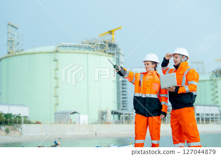 Petrochemical or gas factory workers or technician work in front of tank in factory with one woman point to her right side and one man hold laptop and look to woman pointing direction. 127044879