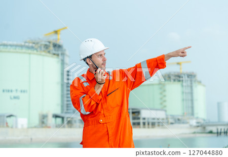 Petrochemical or gas factory worker talk with walkie talkie and point to his left side in front of tank in factory. 127044880