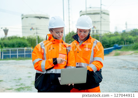 Two factory workers or engineer man and woman work and discuss with laptop in front of factory tank in the workplace. Two factory workers or engineer man and woman work and discuss with laptop in front of factory tank in the workplace. 127044911